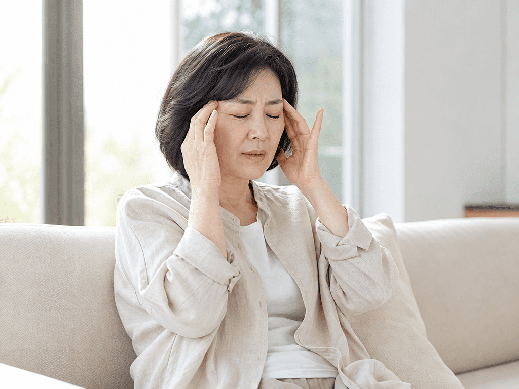 이석증으로 어지럼증을 겪는 중년 여성이 소파에 앉아 양손으로 관자놀이를 짚으며 괴로워하는 모습
