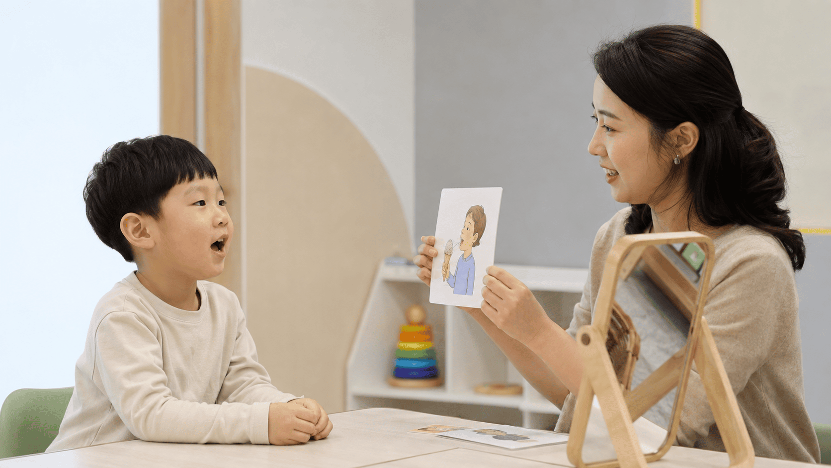 어린 아이가 언어치료사의 그림 카드를 보며 입을 벌려 소리 연습