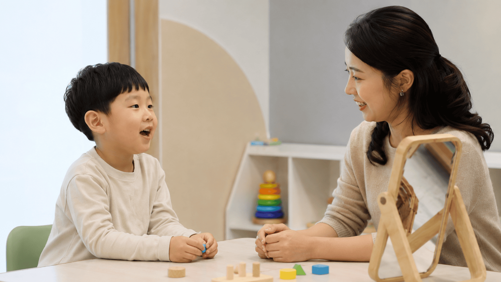 아이가 언어치료사와 마주 앉아 발음 연습하는 밝은 언어치료실.