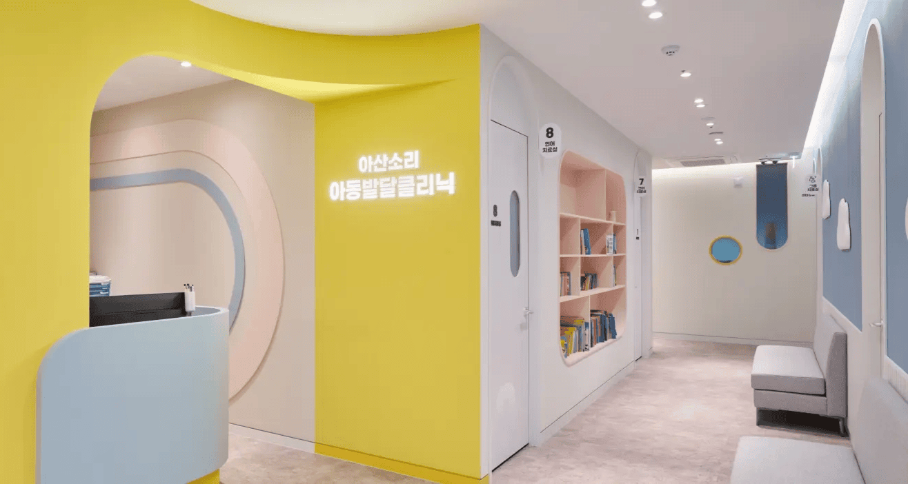 아산소리 아동발달클리닉의 노란색 벽, 파스텔톤 리셉션과 책장 있는 대기 공간.