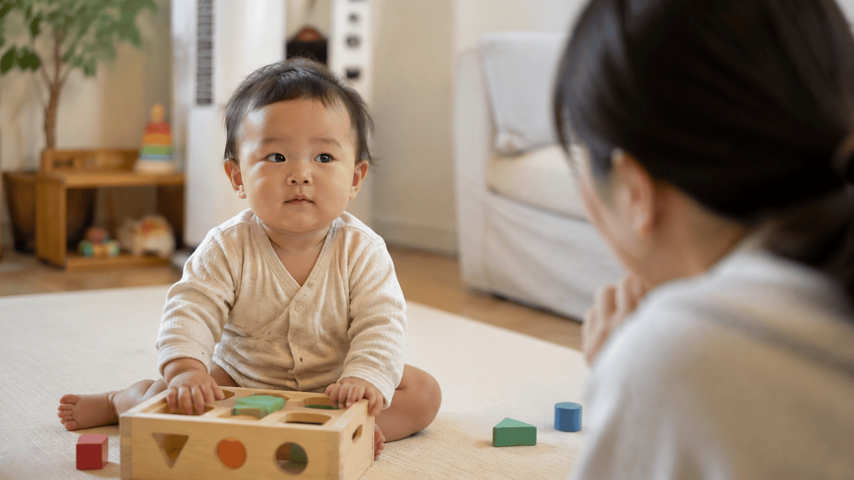 바닥에 앉은 아기가 블록 놀이 중 성인을 바라보고 있다.